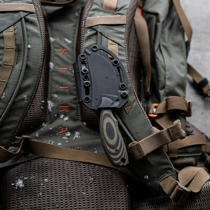 Montana Knife Company's PACKOUT SKINNER in green and black resting on a rugged backpack, showcasing its durable design.