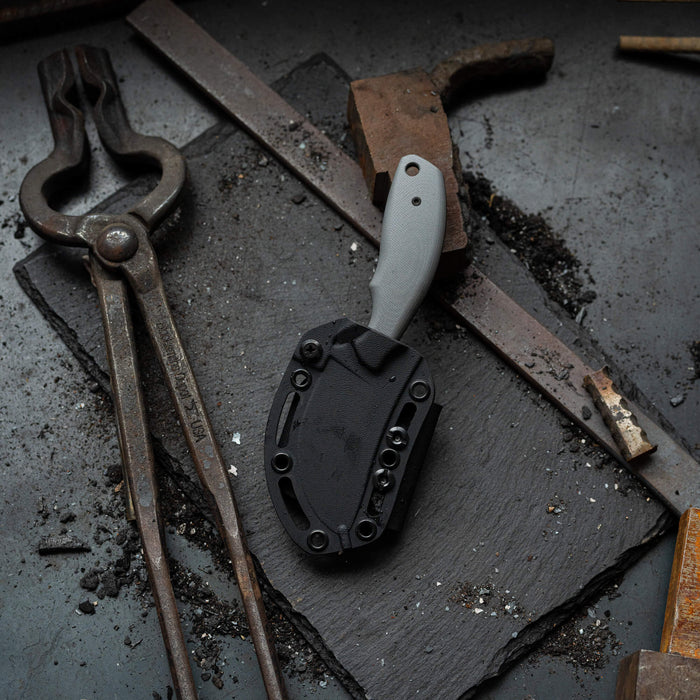 Montana Knife Company's PACKOUT SKINNER in grey, featuring a durable PVD finish, displayed on a textured surface with tools.
