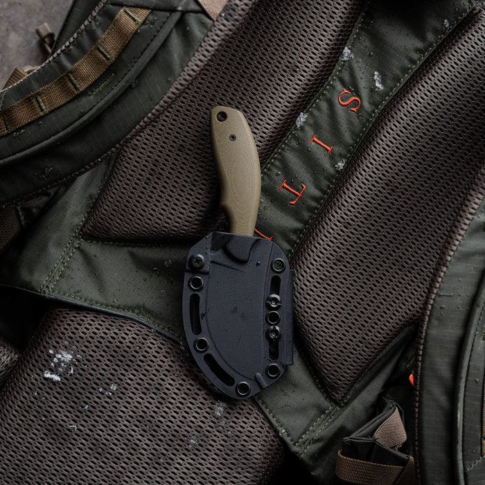 Montana Knife Company's PACKOUT SKINNER in olive, featuring a durable PVD-coated blade, rests on a textured backpack.