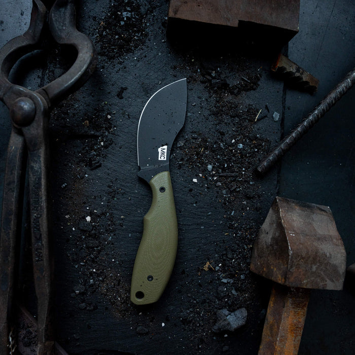Montana Knife Company's PACKOUT SKINNER in olive, featuring a durable PVD-coated blade, set on a textured work surface.