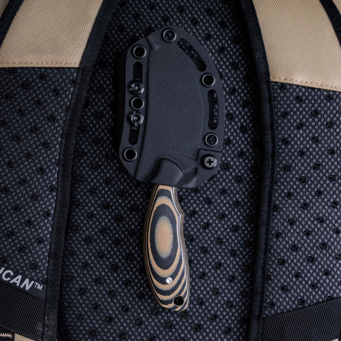 Tan and black PACKOUT SKINNER knife with a textured handle, secured in a tactical backpack.