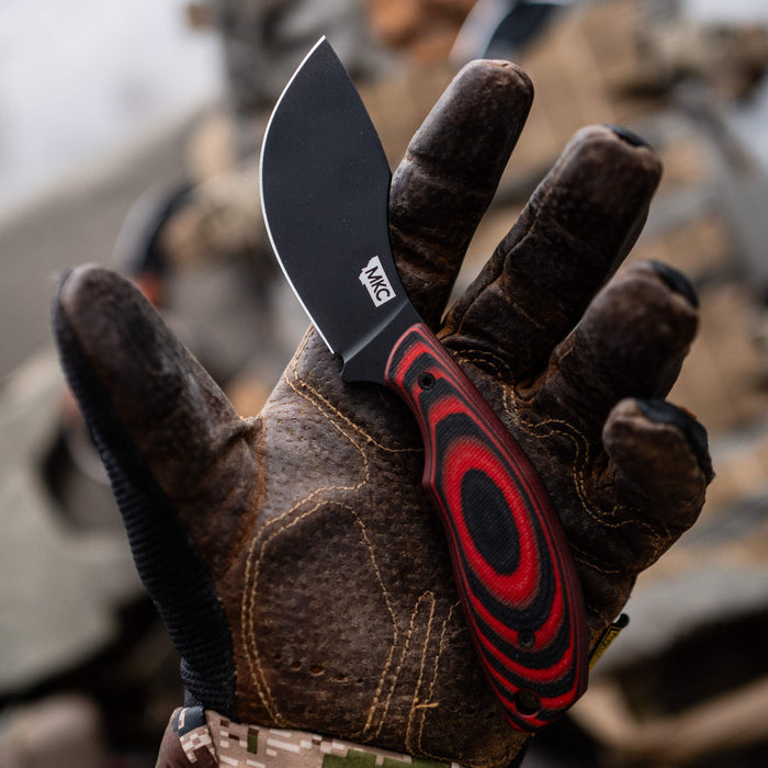 PACKOUT SKINNER PVD knife in red and black, held in a gloved hand, showcasing its sleek design and durable blade.