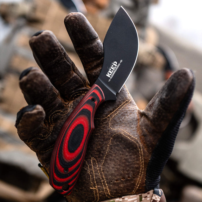 PACKOUT SKINNER PVD knife in red and black, held in a gloved hand, showcasing its sleek design and durable blade.
