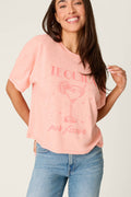 A woman in the P.J. Salvage Paloma Mama Tequila Por Favor Graphic T-Shirt, a grapefruit pink crew tee in soft cotton-modal slub jersey, smiles at the camera. She pairs it with light blue jeans for a comfortable look.