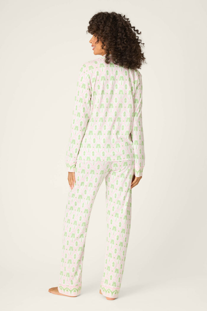 A person with curly hair stands barefoot, facing away, wearing the P.J. Salvage Playful Prints Island Time Long PJ Set in soft cotton-modal jersey with a light green pattern. The background is plain off-white.