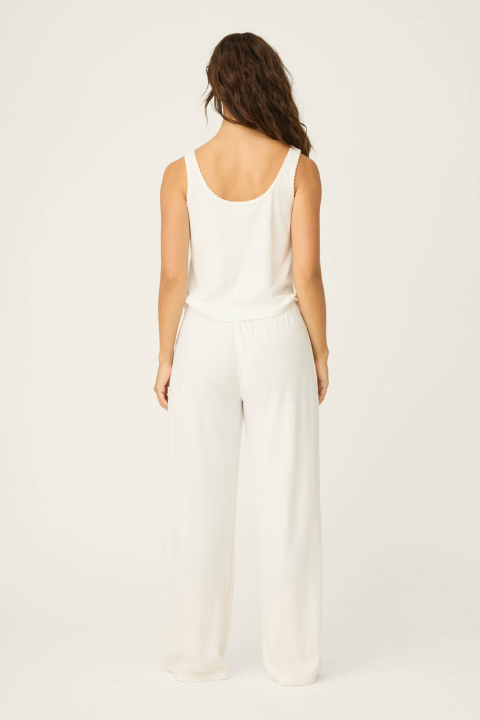 A woman with wavy brown hair, seen from behind, wears the sleeveless white Pointelle Essentials Ivory PJ Set by P.J. Salvage against a plain, light background.