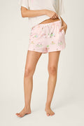 A person stands barefoot in P.J. Salvage Pupcation Palms Sunnies & Sunshine PJ Shorts—light pink with small colorful prints—in a runner-style fit and a loose white t-shirt, left hand in pocket, head not visible.