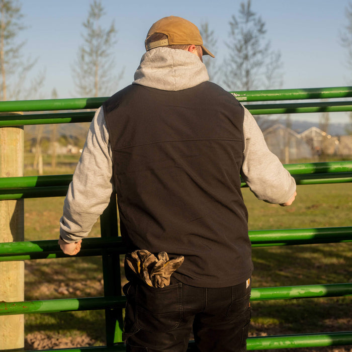 Man wearing a black Rexford Ripstop vest with gray sleeves, working on a green fence in an outdoor setting.