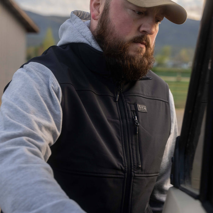 Man wearing a black Rexford Ripstop Vest over a gray hoodie, preparing to enter a vehicle outdoors.