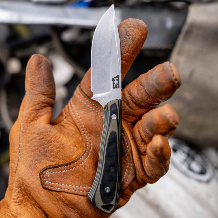 Green and black ROCKER knife held in a gloved hand, showcasing its compact blade and ergonomic handle design.