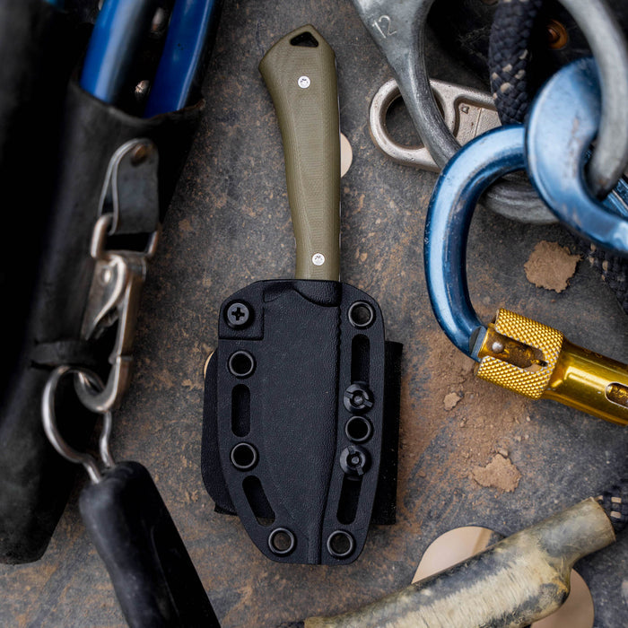 Olive green ROCKER knife with a black sheath, surrounded by climbing gear and tools, showcasing its rugged design.