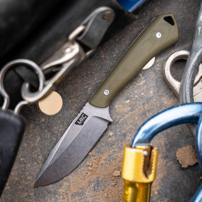 Olive green fixed-blade knife with a rugged design, placed among tools on a work surface. Ideal for outdoor and tactical use.