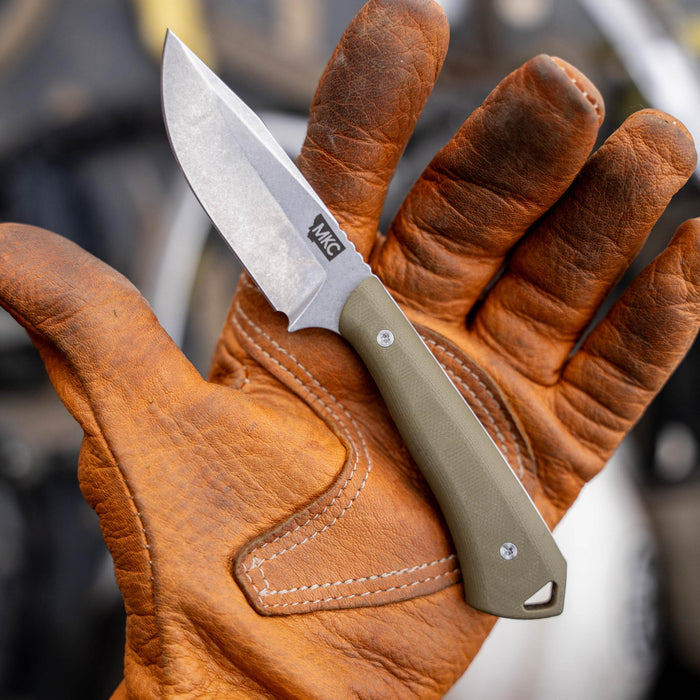 Olive green ROCKER knife held in a gloved hand, showcasing its durable blade and ergonomic handle design.