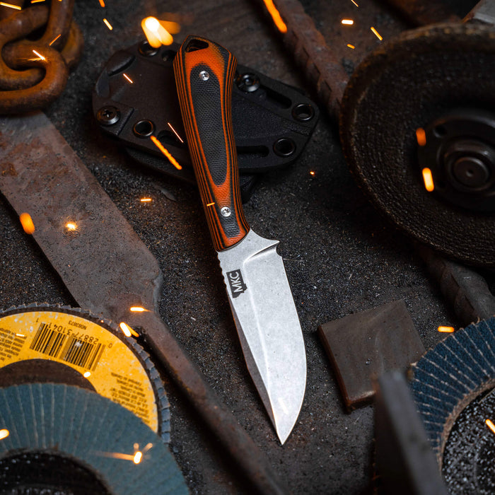 ROCKER knife in orange and black, featuring a sleek blade and textured handle, set against a backdrop of tools and sparks.