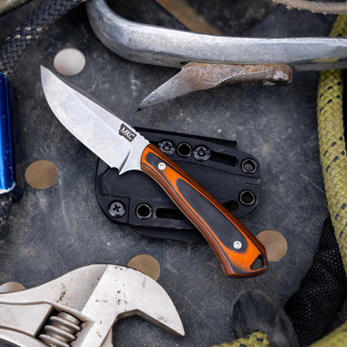 Rocker knife in orange and black resting on a tool surface, showcasing its durable design and sharp blade.