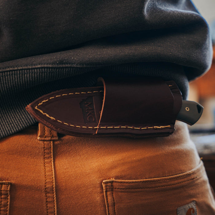 Horizontal leather sheath for knives, securely attached to a belt, showcasing rugged craftsmanship and functionality.