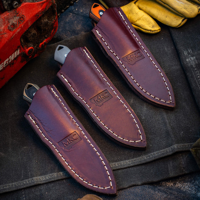Three ROCKER leather sheaths for vertical belt carry, showcasing durable craftsmanship and MKC branding.