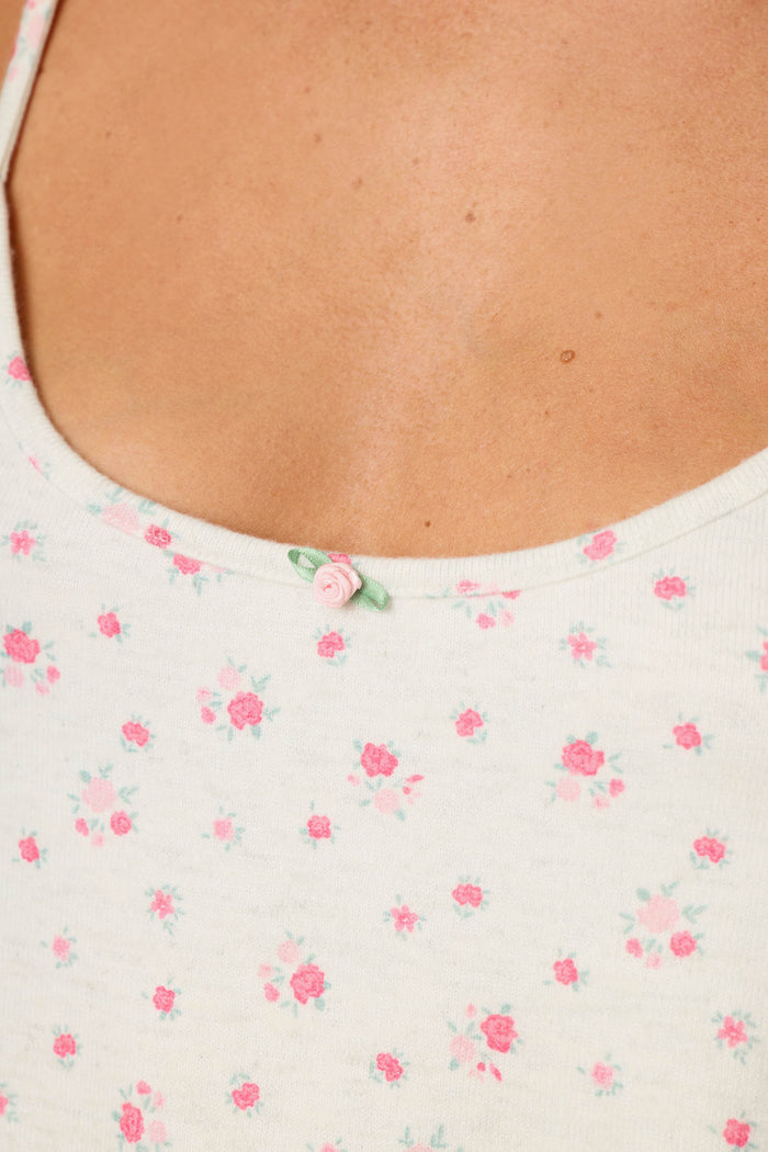 Close-up of a person wearing the P.J. Salvage Romantic Rose Ditsy Rose Print Camisole, a white tank top featuring small pink floral prints and a delicate pink rosette decoration at the neckline.
