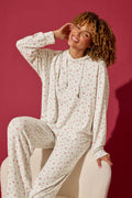 A smiling person with curly hair sits on a chair against a solid maroon background, wearing the P.J. Salvage Romantic Rose Ditsy Rose Print Hoodie and matching pants.