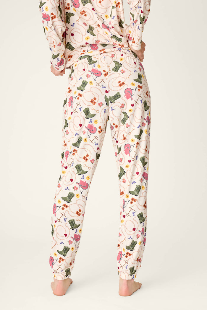 A person standing barefoot, shown from the back, wearing P.J. Salvage Saddle Up Western Print Pajama Jogger Pants featuring a colorful floral and leaf pattern.