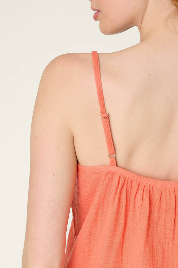 A close-up of a person's back and shoulder wearing a sleeveless top with thin adjustable straps, against a plain light background.