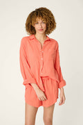 A person stands against a plain background wearing the P.J. Salvage Sea You in Capri Hot Coral Nightshirt with a front pocket. Their curly hair is styled naturally and their expression is neutral.