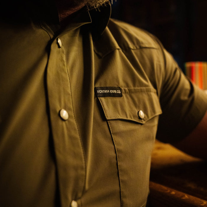 Olive short-sleeve button-up shirt from Montana Knife Company featuring a chest pocket and logo detail.