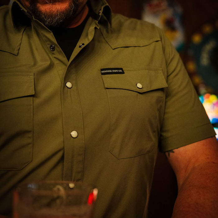 Olive short-sleeve button-up shirt from Montana Knife Company, featuring two chest pockets and a relaxed fit.