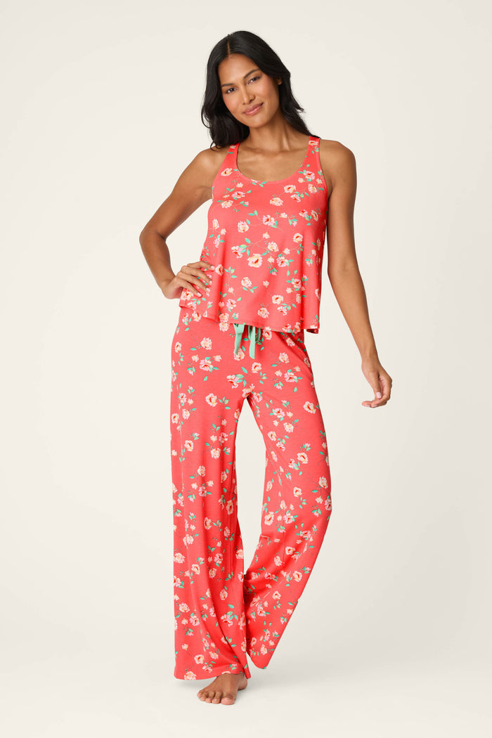 A woman wearing the P.J. Salvage Siesta Dreams Dark Coral Floral Print Tank Top stands smiling with one hand on her hip against a plain light background, paired with wide-leg pajama pants in soft modal jersey.