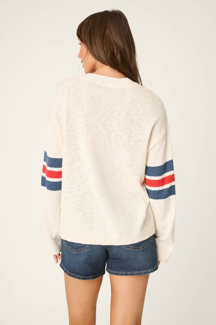A person with long brown hair stands with their back to the camera, wearing a star and stripe patterned sweater and denim shorts.