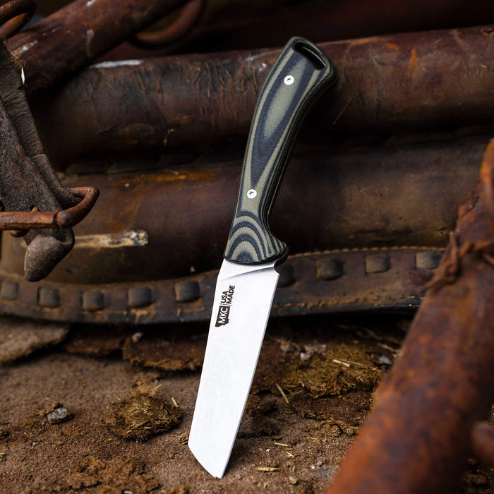 Stockyard knife in green and black handle resting on rustic metal and dirt background, showcasing its durable design.