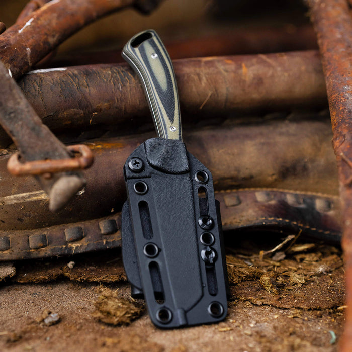 Stockyard knife in green and black with a durable sheath, resting on rustic metal and dirt background.
