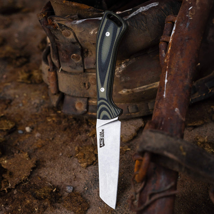 Stockyard knife with a green and black handle, featuring a durable blade, resting on rugged terrain.