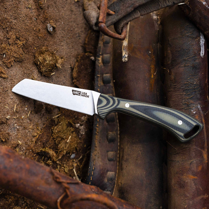 Stockyard knife in green and black handle, featuring a stainless steel blade, placed on rustic leather and dirt background.