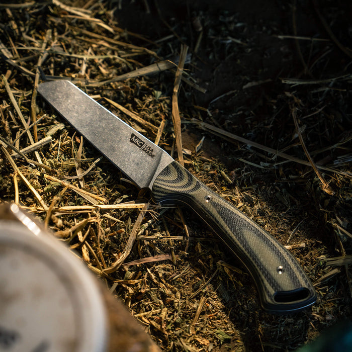 Stockyard knife in green and black with a textured handle, resting on straw and dirt, showcasing its rugged design.