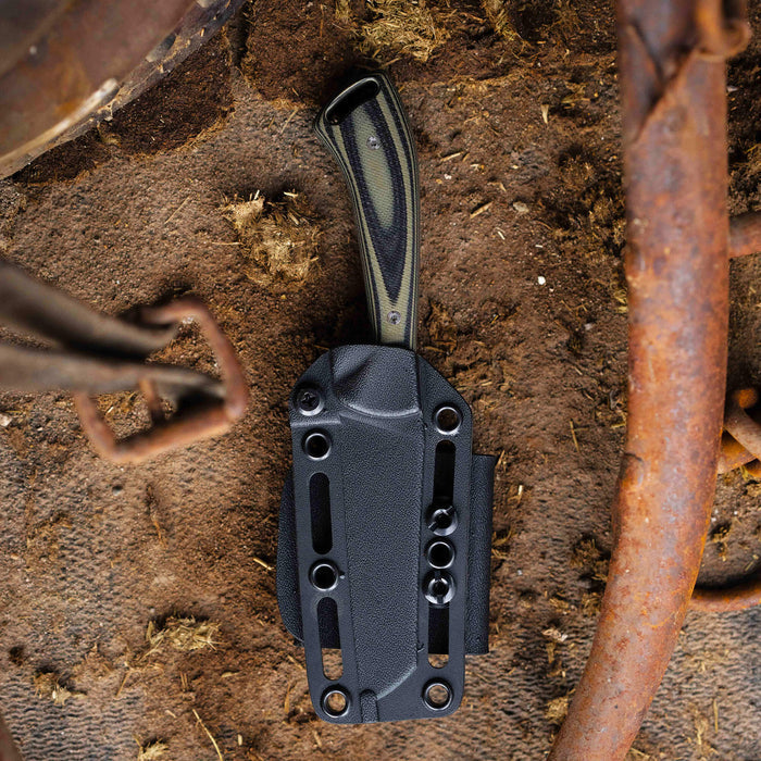 Stockyard knife in green and black sheath resting on dirt, showcasing durable design for outdoor use.