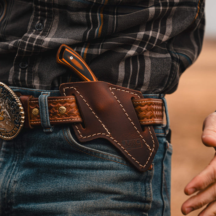 Angled leather sheath for knife, securely attached to a belt, showcasing craftsmanship and practicality for outdoor use.