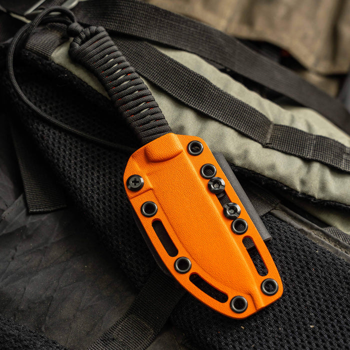 Orange Kydex sheath for the Stoned Goat 2.0 knife, featuring a secure design and attachment points, resting on tactical gear.
