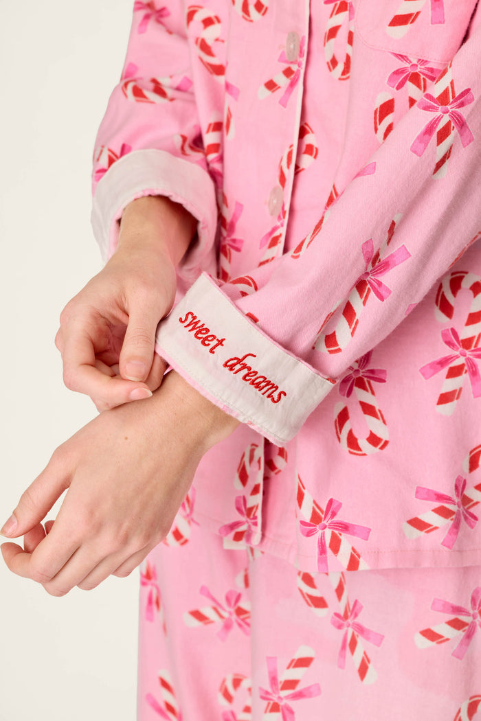 A person wearing the P.J. Salvage Sweeter Than Sugar Candy Cane Print 4-Piece PJ Set rolls up a sleeve featuring “sweet dreams” embroidered in red on the white cuff; only their hands and torso are visible.