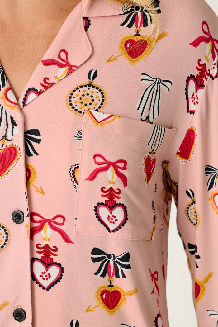 Close-up of the P.J. Salvage Sweetheart Dreams Love Lockets Print Nightshirt, a pink button-up shirt with a pocket, featuring a charming pattern of hearts with bows, dotted circles, and black-and-white bows.