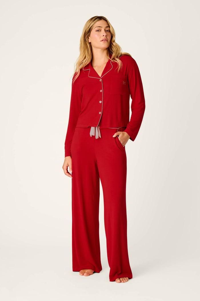 A woman stands barefoot against a plain light background, wearing the P.J. Salvage Sweetheart Dreams Red Long Sleeve PJ Set, which features white trim on the collar and buttons.