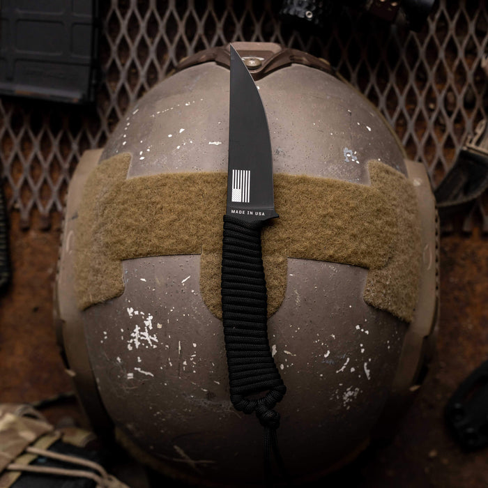 Tactical Speedgoat knife in black finish resting on a tactical helmet, showcasing its sleek design and durable construction.