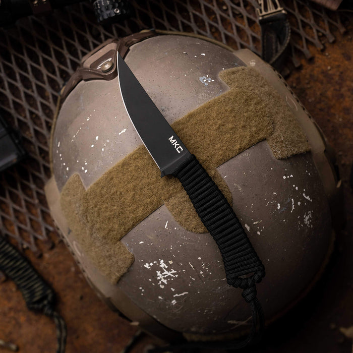Tactical Speedgoat knife in black with a textured handle, resting on a tactical helmet background.