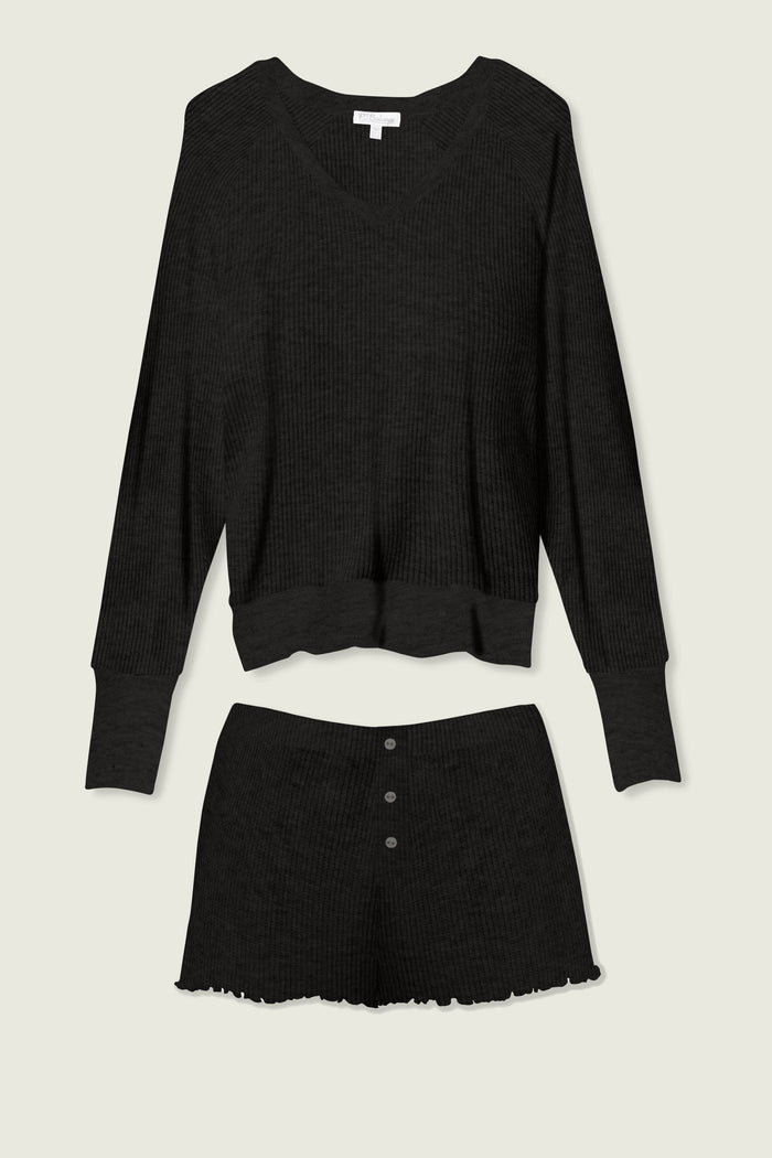 The P.J. Salvage Textured Essentials Black Short Lounge Set features a ribbed knit V-neck long-sleeve top and high-waisted shorts with three buttons and a ruffled hem, shown laid flat on a light background.