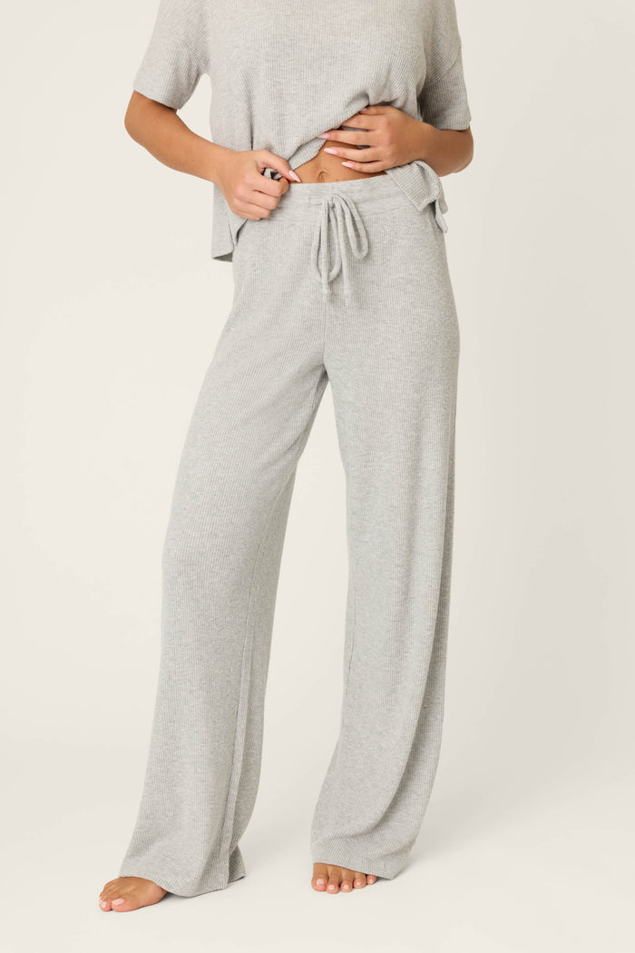 A person wearing P.J. Salvage Textured Essentials Heather Grey Open Leg Pants with a short-sleeve top. The ribbed knit loungewear set is loose-fitting; the person is barefoot and their face isn't visible.