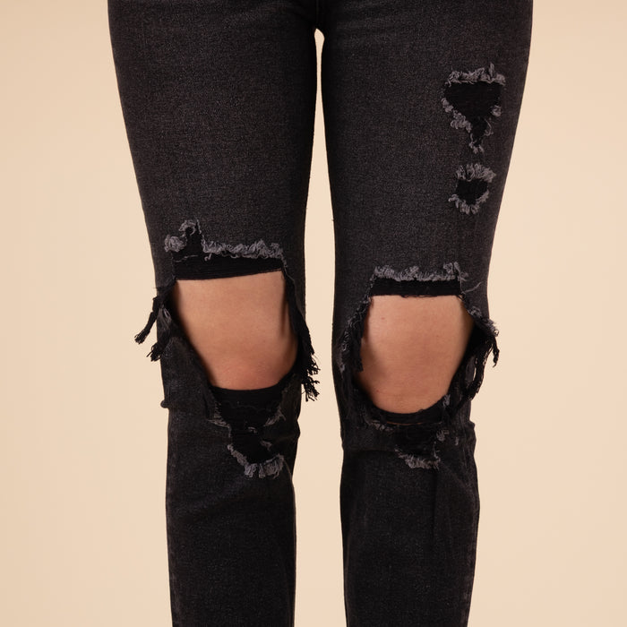 Close-up of the distressed knee area, showing frayed edges and worn-in texture on the black denim fabric.