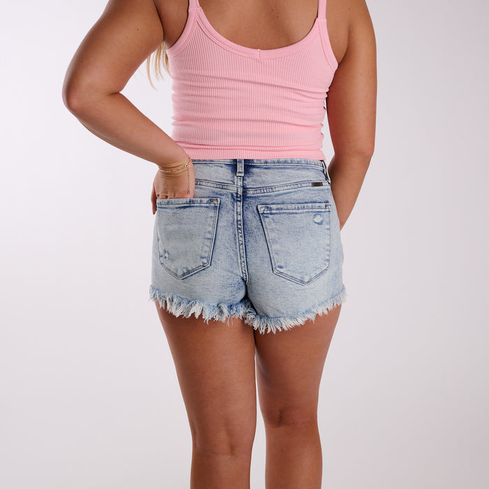 Medium wash high-rise distressed denim shorts with raw frayed hem shown from back view.