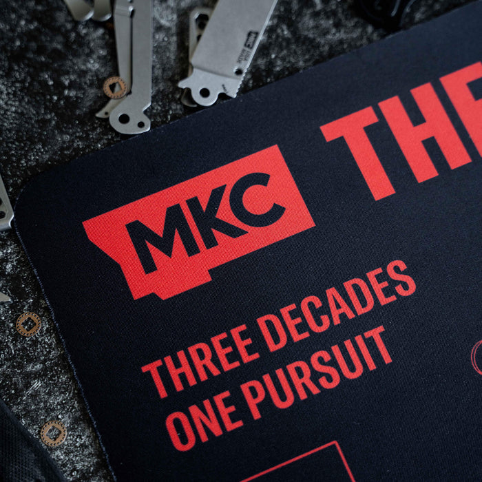 Close-up of the Montana Desk Mat featuring the MKC logo and the text "Three Decades One Pursuit," designed for durability.