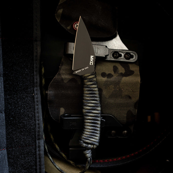 Black and dark camo TRAIL GOAT knife with a sleek blade and paracord handle, showcasing its tactical design.