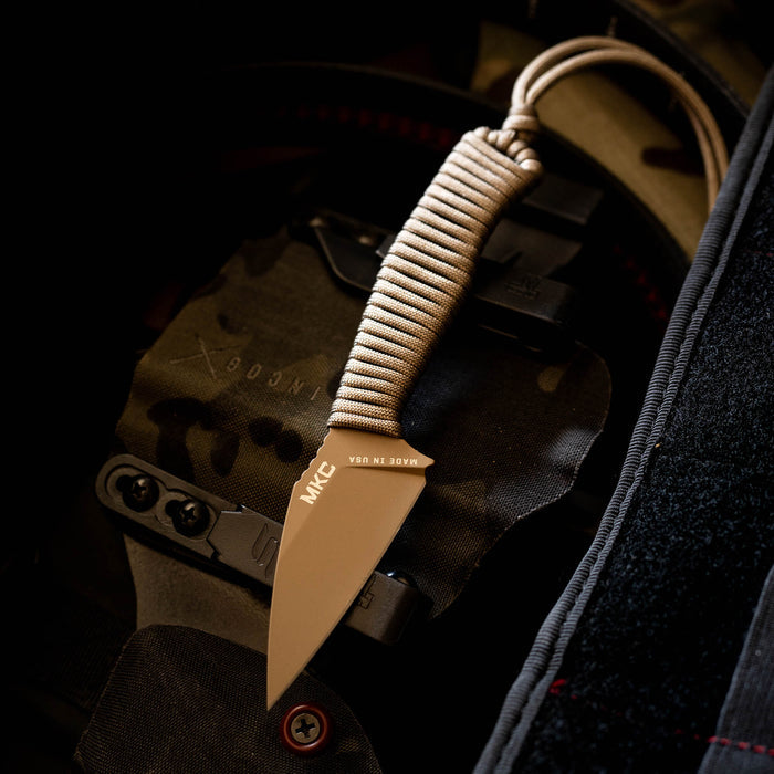 TRAIL GOAT knife with a coy/olive drab handle, featuring a compact blade and paracord wrap, resting on tactical gear.